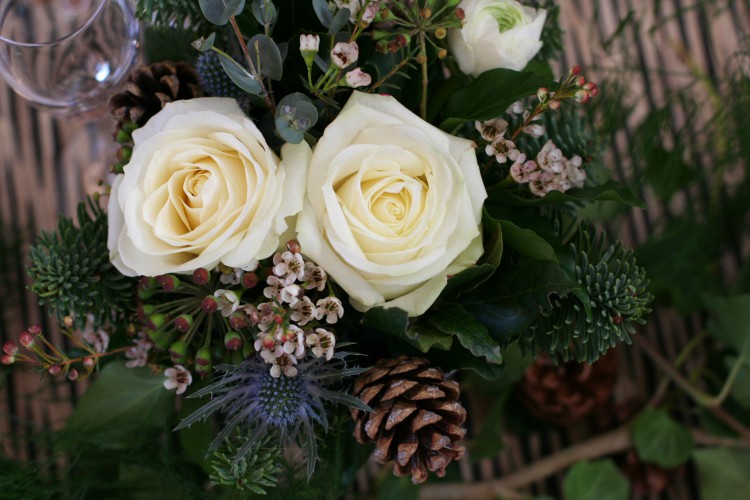 winter table arrangement with ivory roses, pine cones, thistles , waxflower and eucalyptus